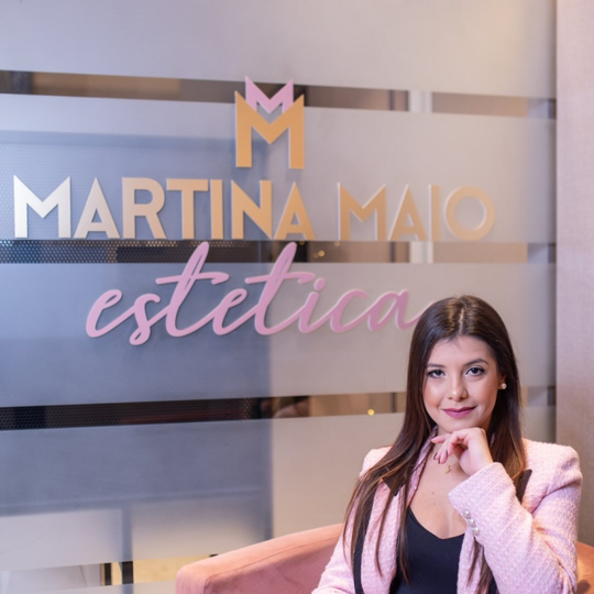 Una professionista in posa con un blazer rosa davanti a un'insegna in vetro satinato con la scritta