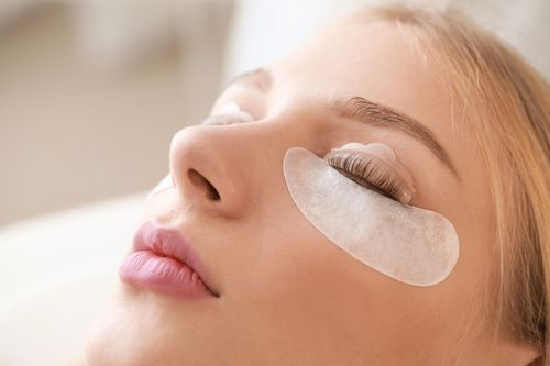 Una persona sdraiata con un cuscinetto protettivo bianco sotto la palpebra durante l'applicazione di extension per ciglia.