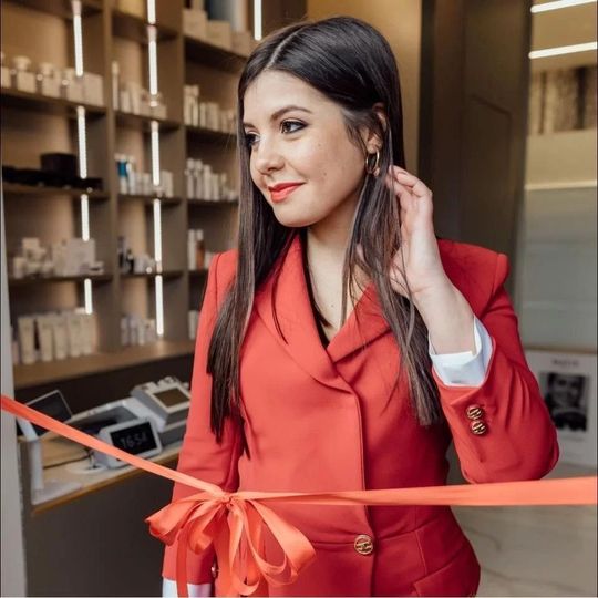 Una persona che indossa un blazer rosso taglia un nastro rosso cerimoniale in una spa o in un negozio.