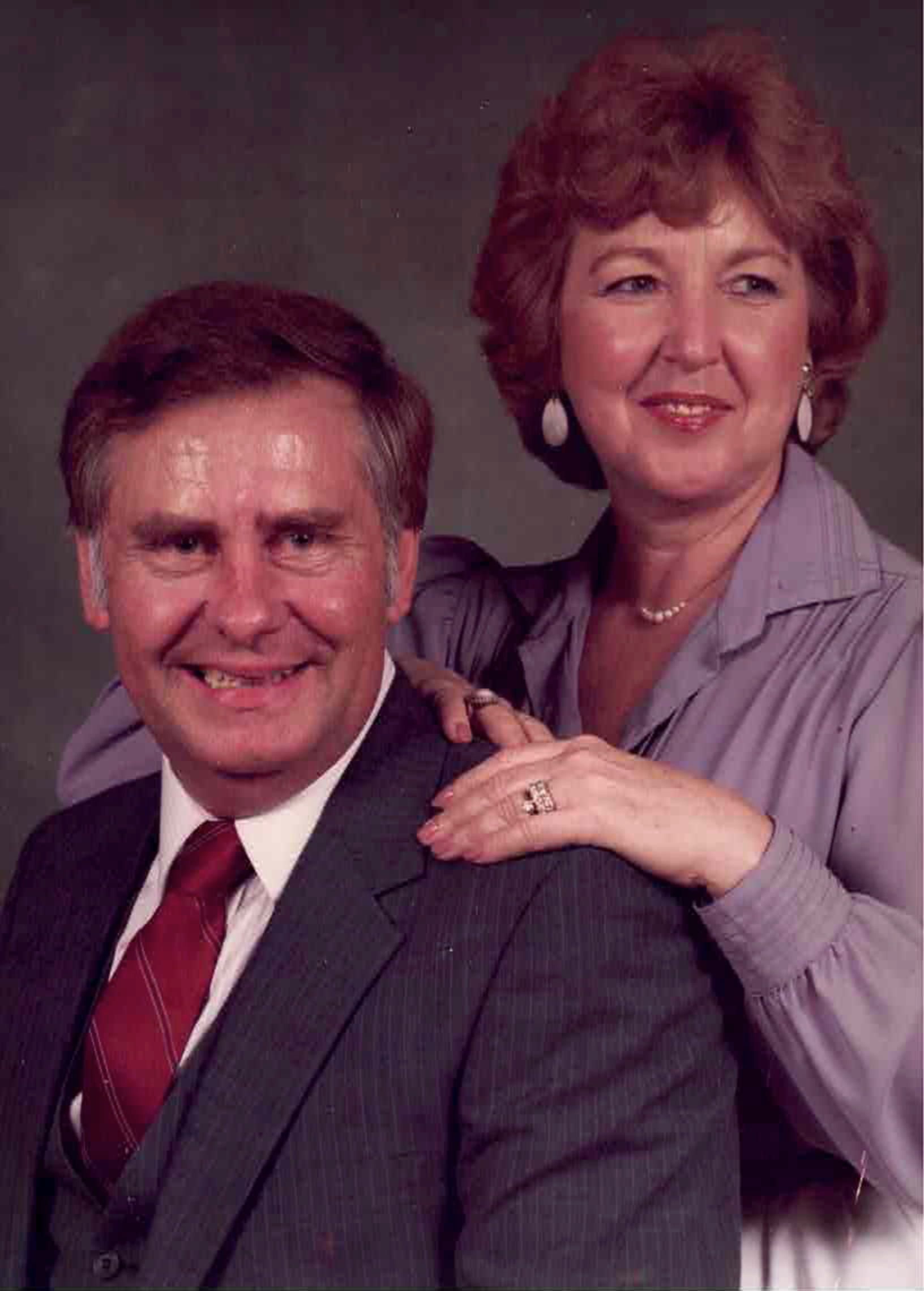 A man in a suit and tie is standing next to a woman in a purple shirt