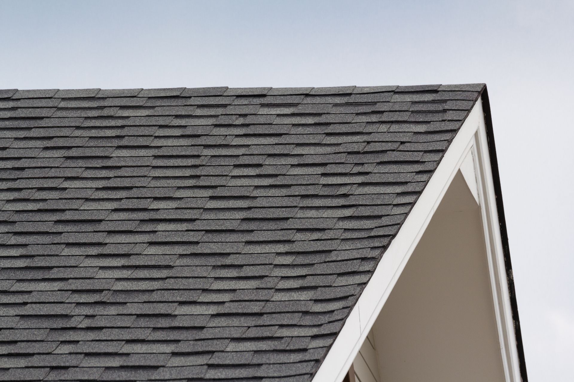 Gray asphalt shingle roof close-up under clear sky – residential roofing texture and materials.