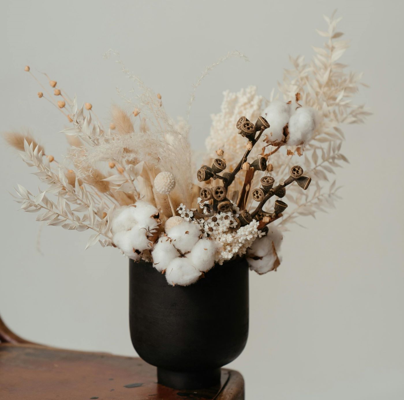 A black vase filled with dried flowers is sitting on a wooden table.