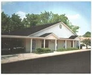 A white house with a black roof and a car parked in front of it.