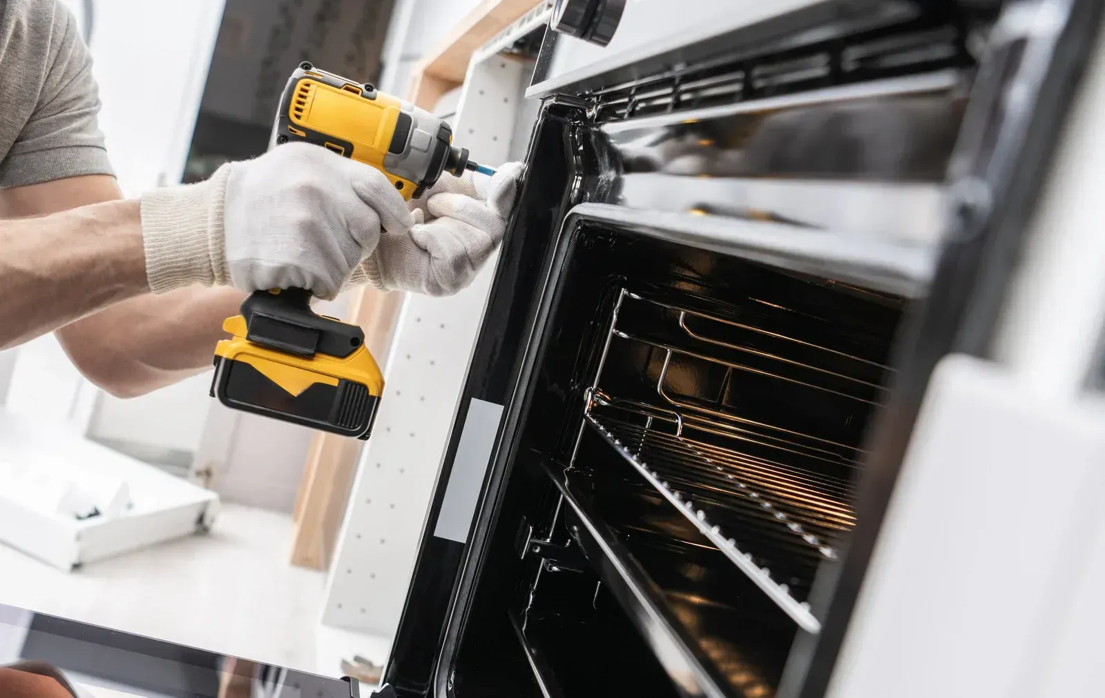 Person in gloves using a yellow drill to work on an oven.