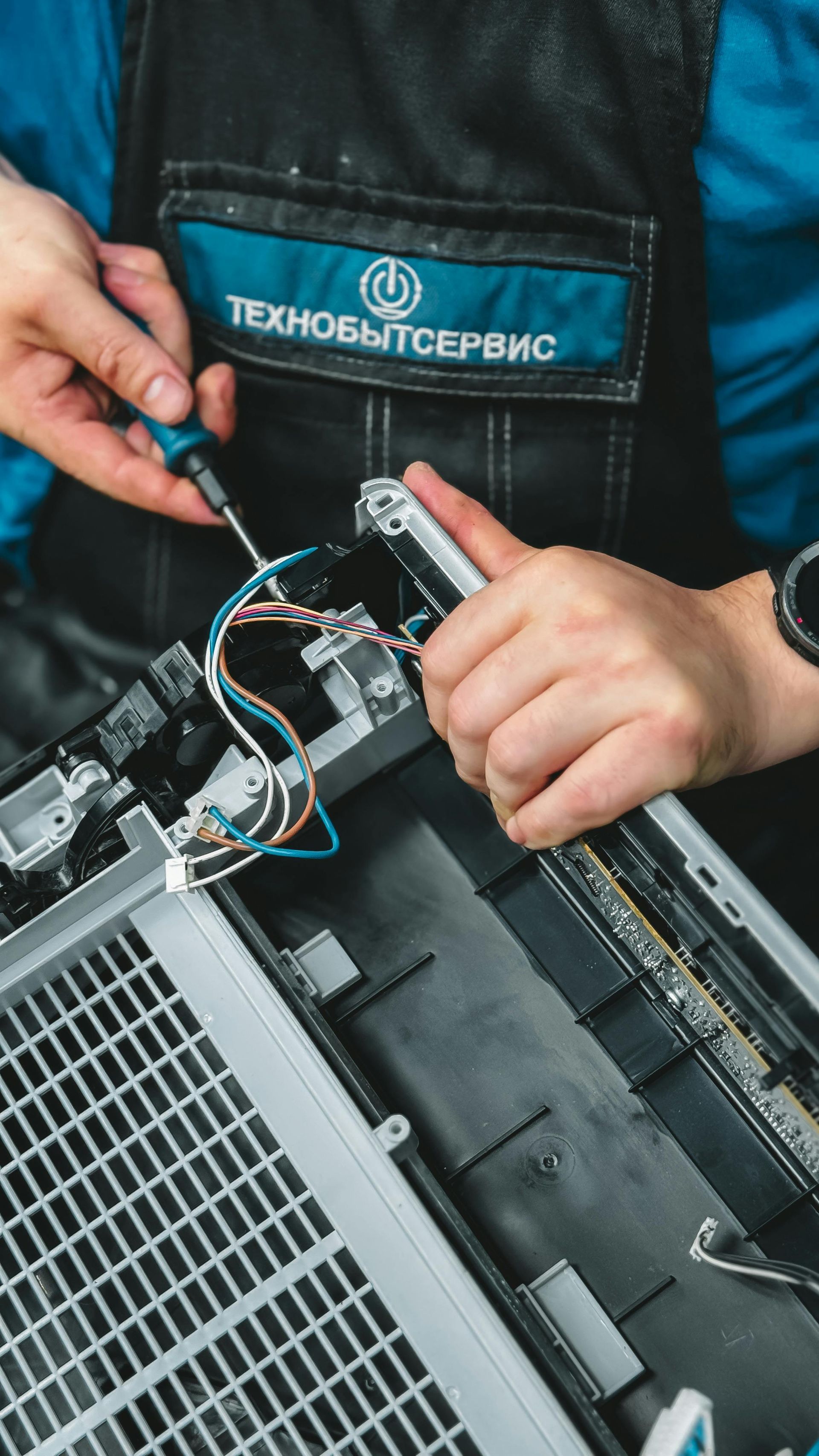 Person in apron using a screwdriver on electronic equipment. Blue and black wires are visible.