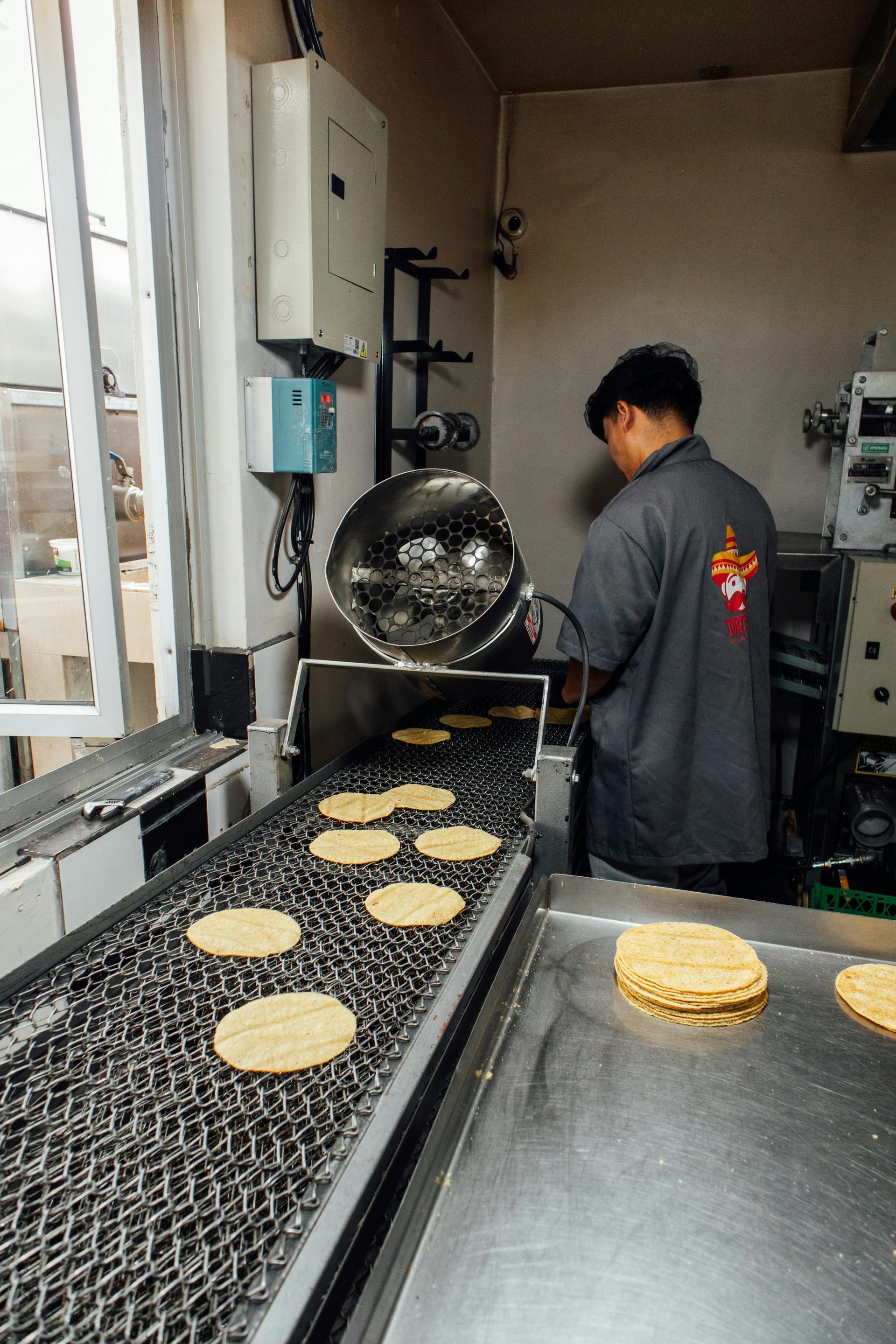 Person placing flatbread onto a conveyor belt in a commercial kitchen.