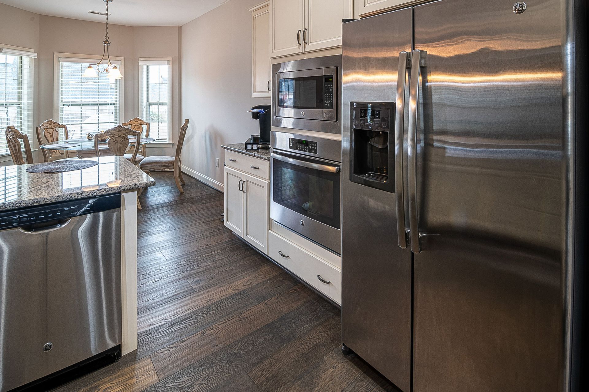 Bright modern kitchen with stainless steel appliances, white cabinets, and a dining table by the window
