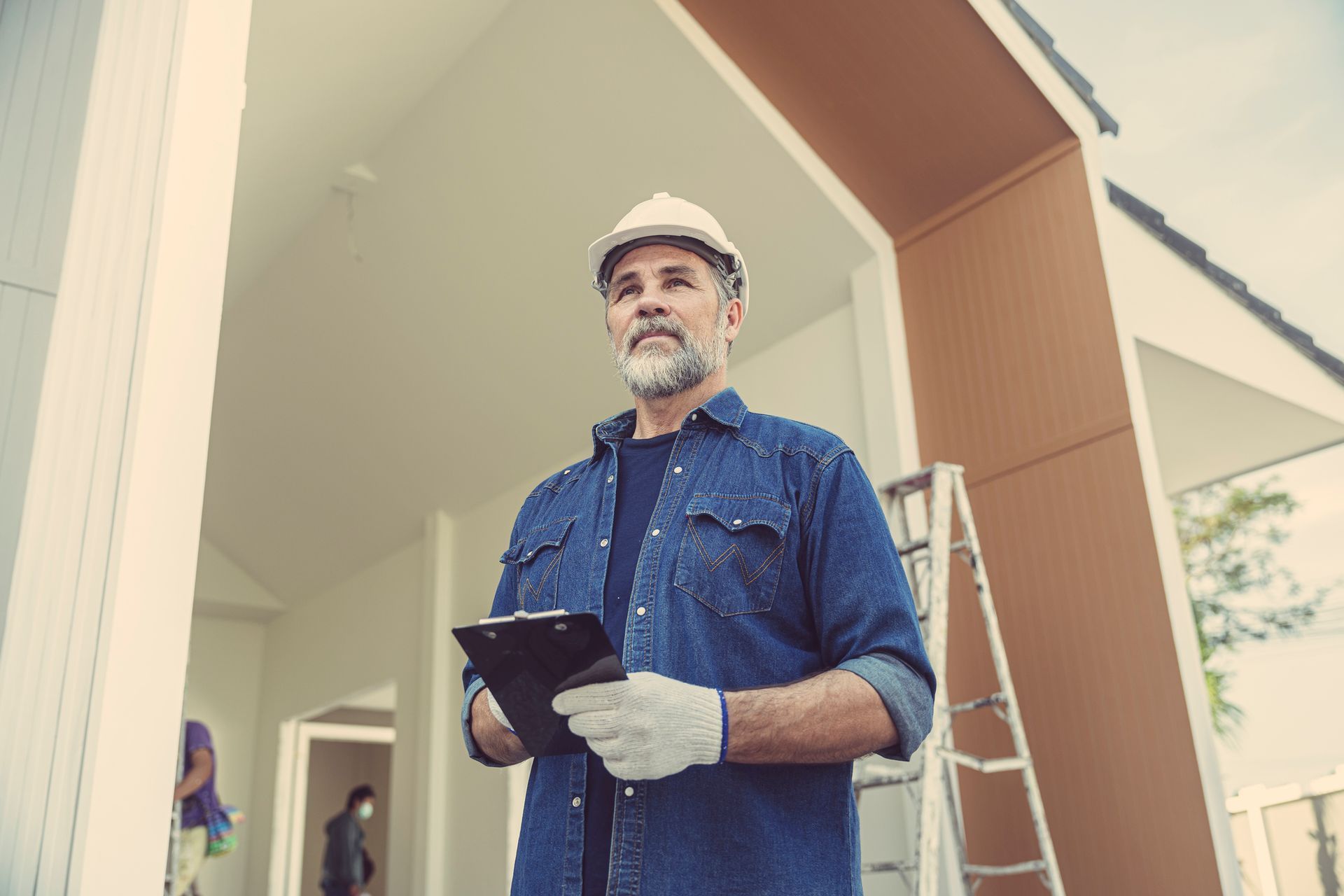 Construction worker in hard hat and gloves, holding a clipboard, inspecting a building's interior.