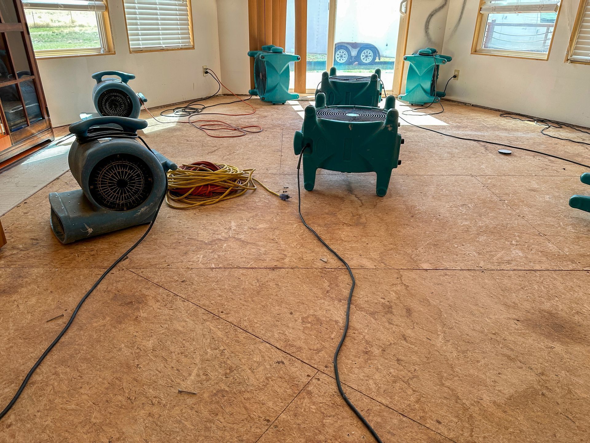 Room with several large fans drying the particle board floor after water damage.