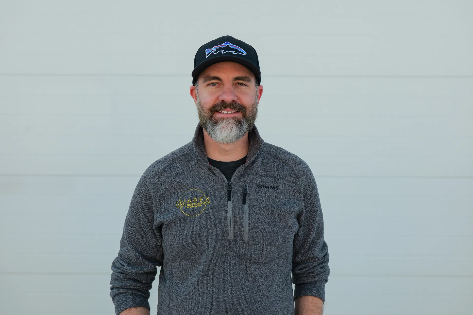Woman with dark curly hair smiles, eyes closed, hand in hair, wearing polka dot top.