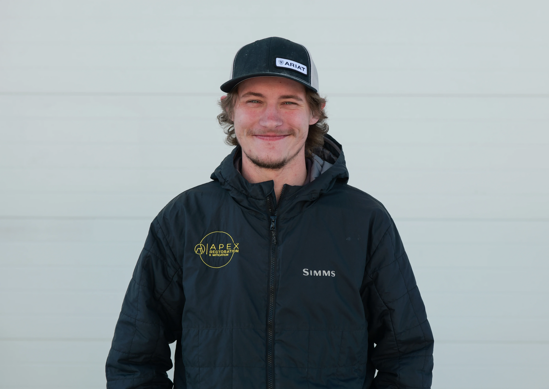Woman with dark curly hair smiles, eyes closed, hand in hair, wearing polka dot top.