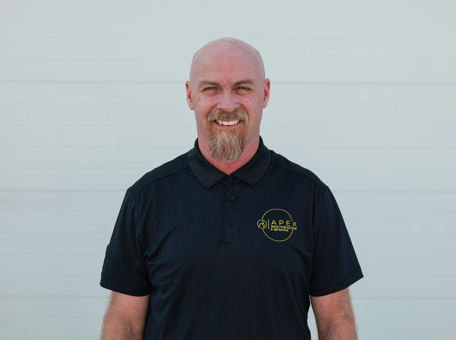Woman with dark curly hair smiles, eyes closed, hand in hair, wearing polka dot top.