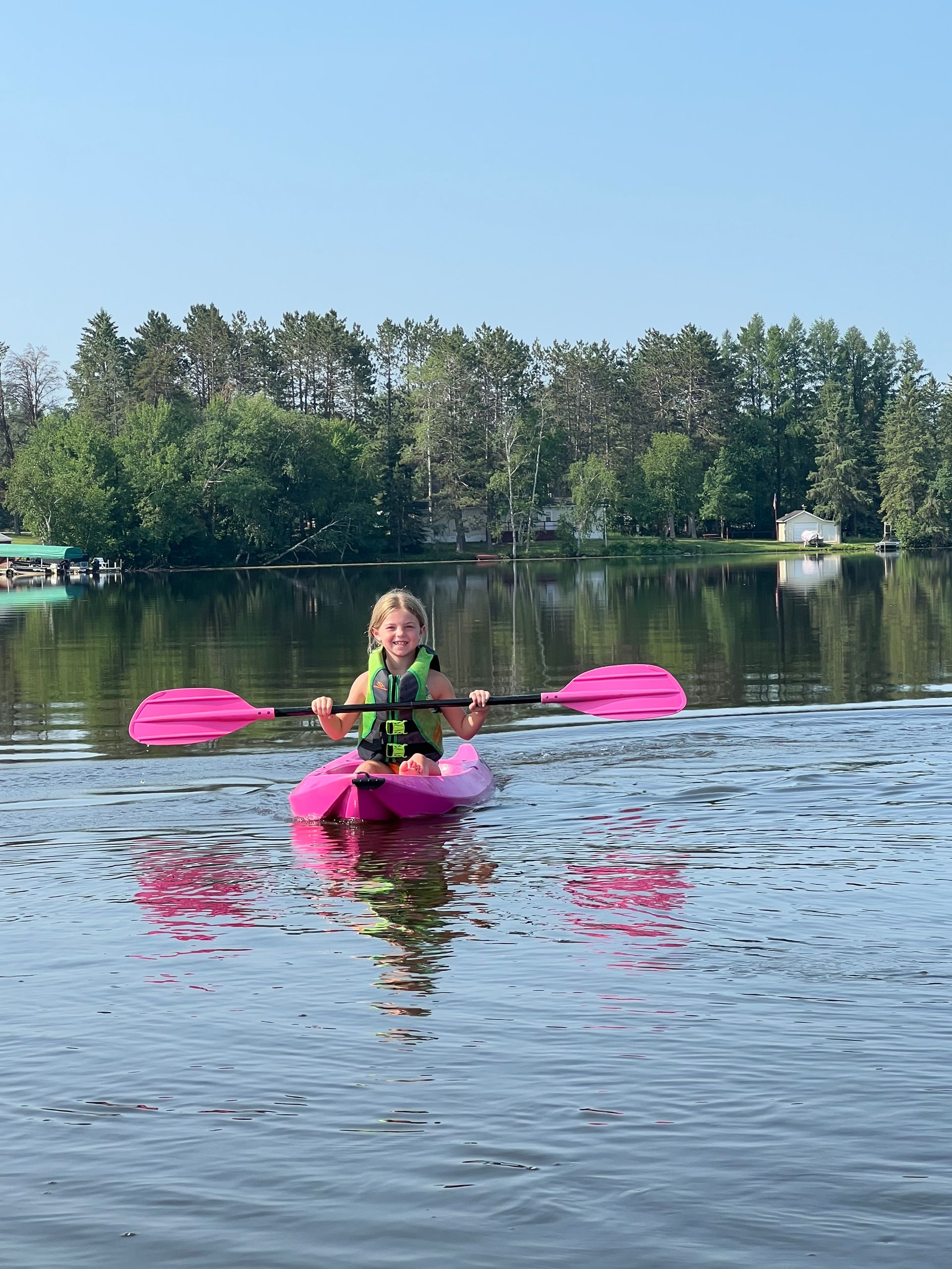 A little girl is riding a pink kayak on a lake.
