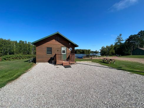 A small wooden cabin with a gravel driveway in front of it.