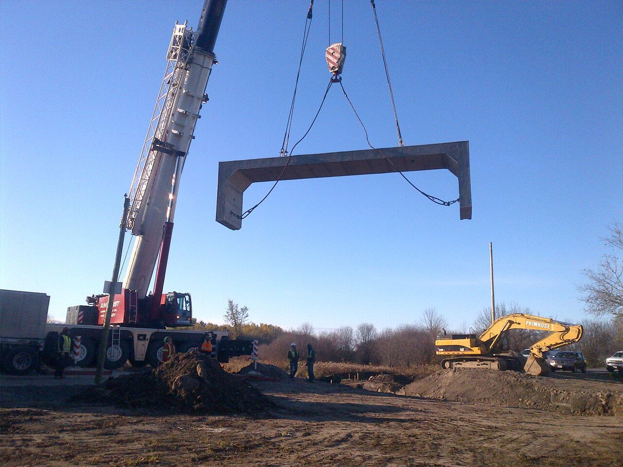 A crane lifts a concrete bridge segment above a construction site.