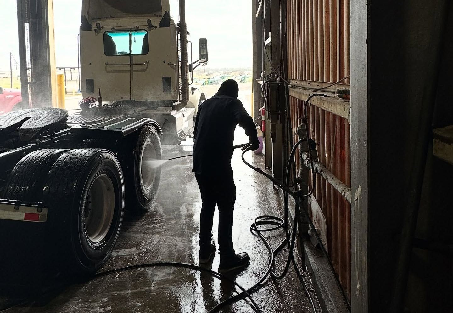 A man is washing a semi truck in a garage. A man is washing a semi truck in a garage.