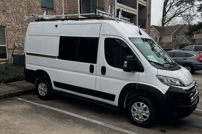 A white van is parked in a parking lot in front of a building. A white van is parked in a parking lot in front of a building.