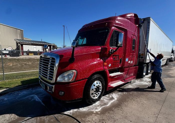A man is washing a red semi truck with a hose. A man is washing a red semi truck with a hose.