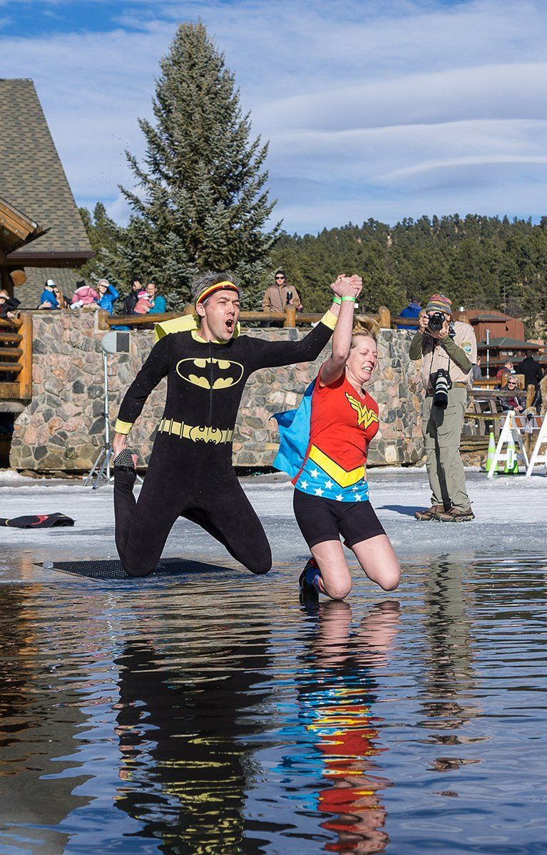 Batman and Wonder Woman in costumes in icy water, raising arms, with onlookers.