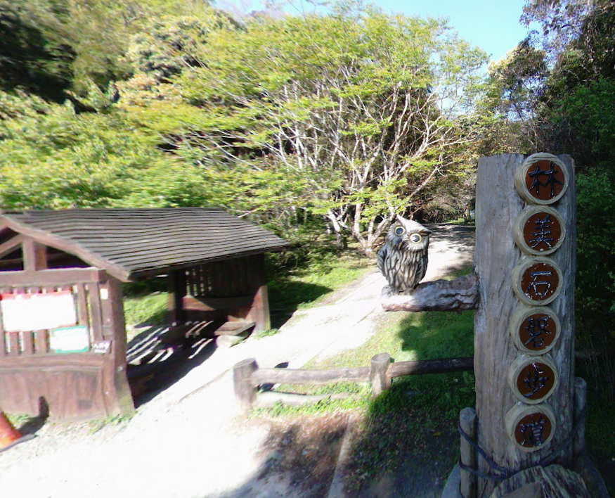 Entrance to a trail, with wooden shelter, post with markers, and hiker walking on path.