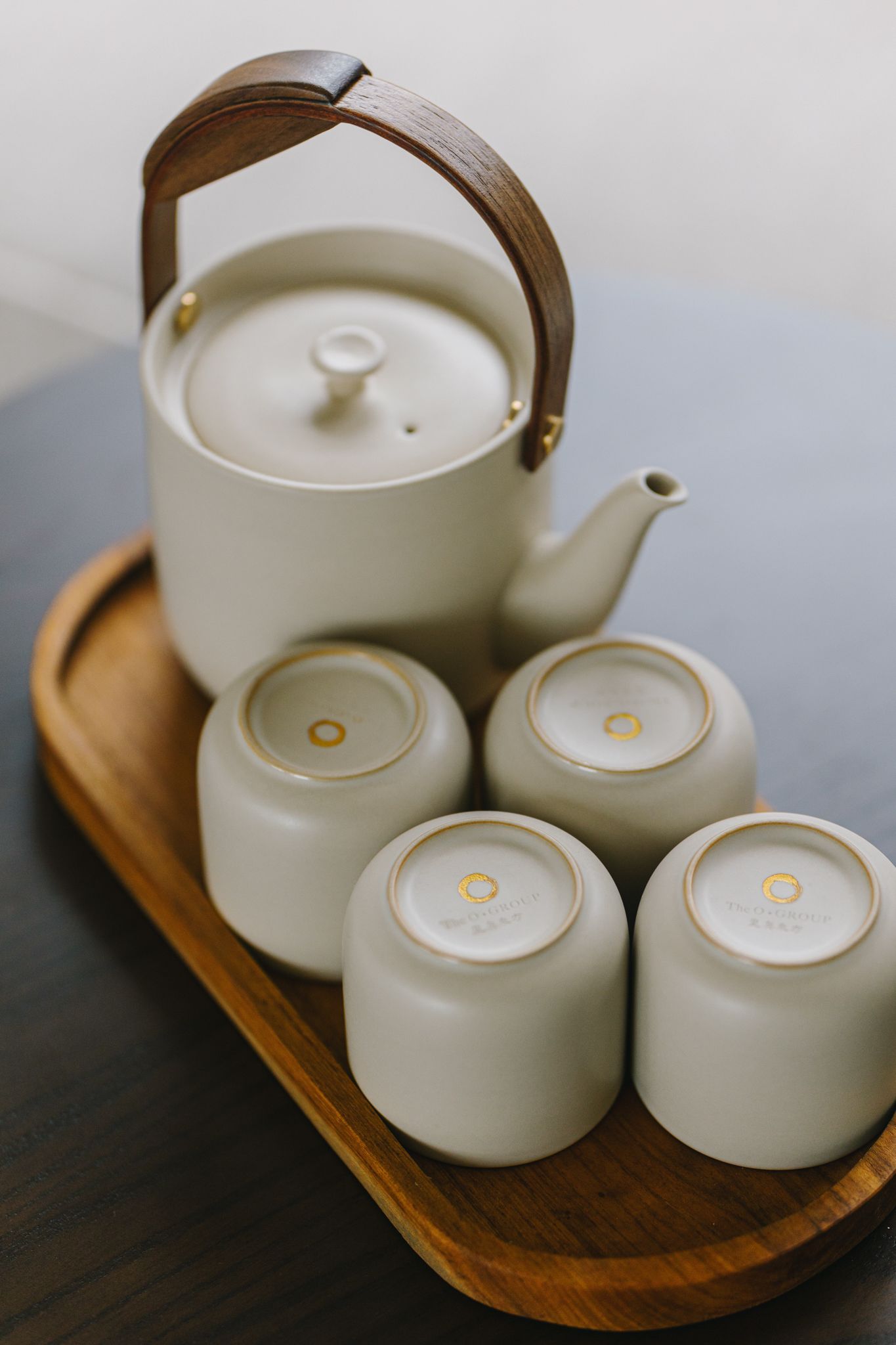 Cream-colored tea set with wooden handle and cups on a wooden tray, set on a dark surface.