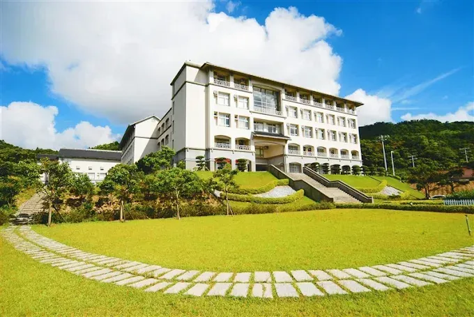 Hotel building with grassy lawn, trees, and cloudy blue sky.