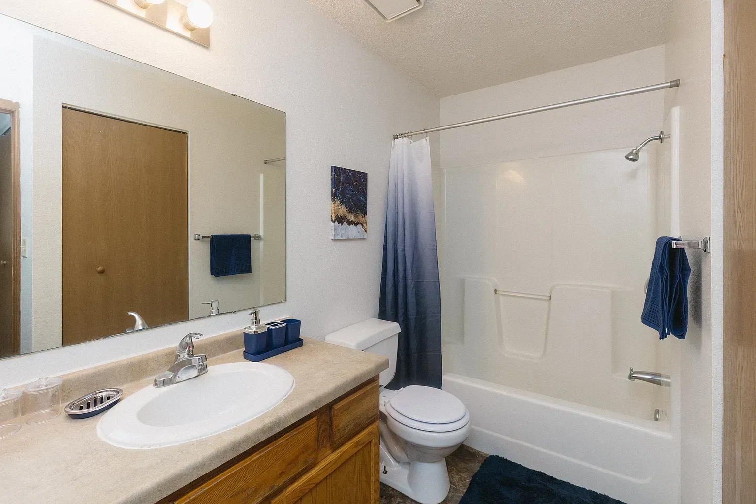 Bathroom with a white bathtub, toilet, and sink. Blue ombre shower curtain and towels. Light wood vanity.