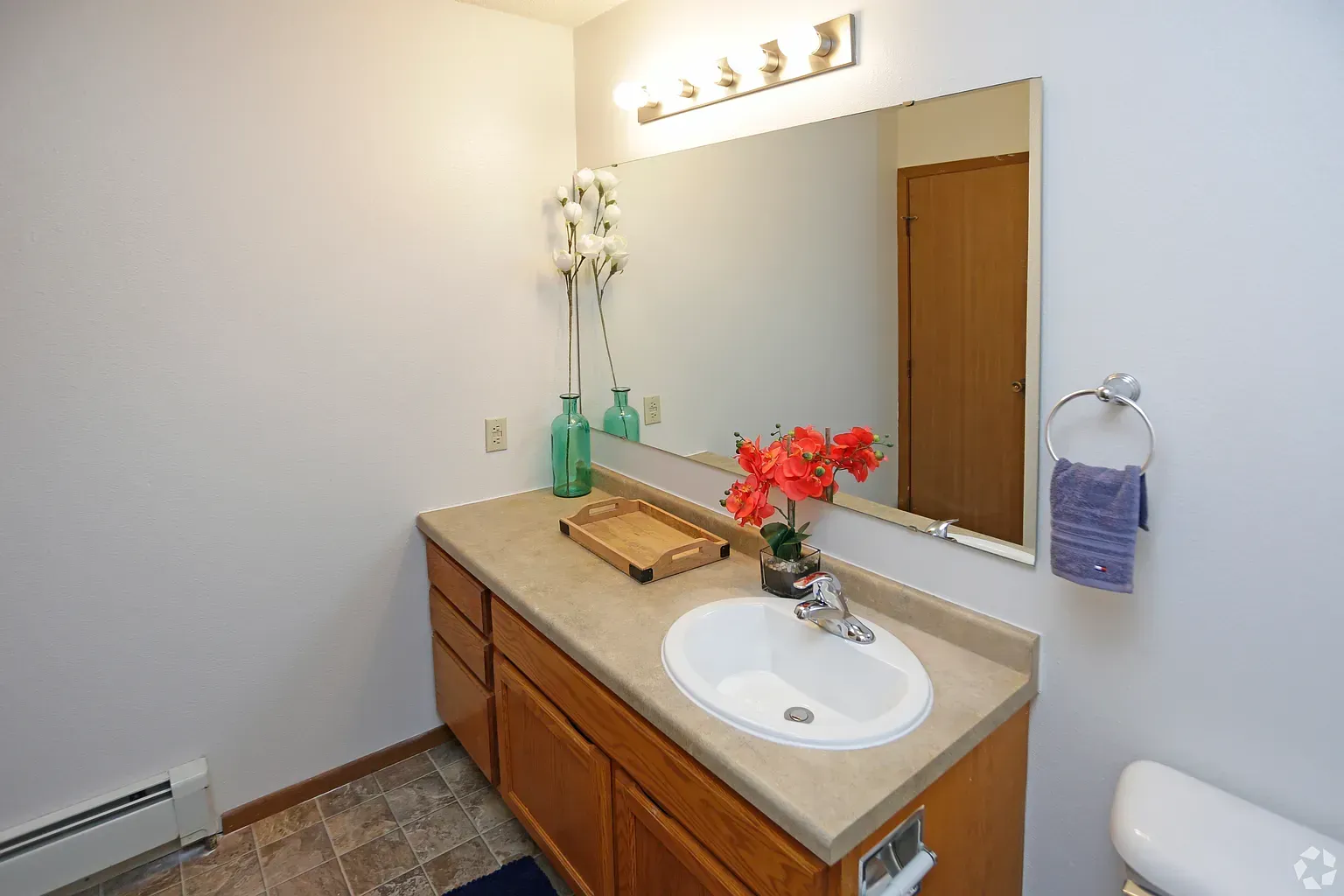 Bathroom with wooden vanity, oval sink, large mirror, and decorative flowers.