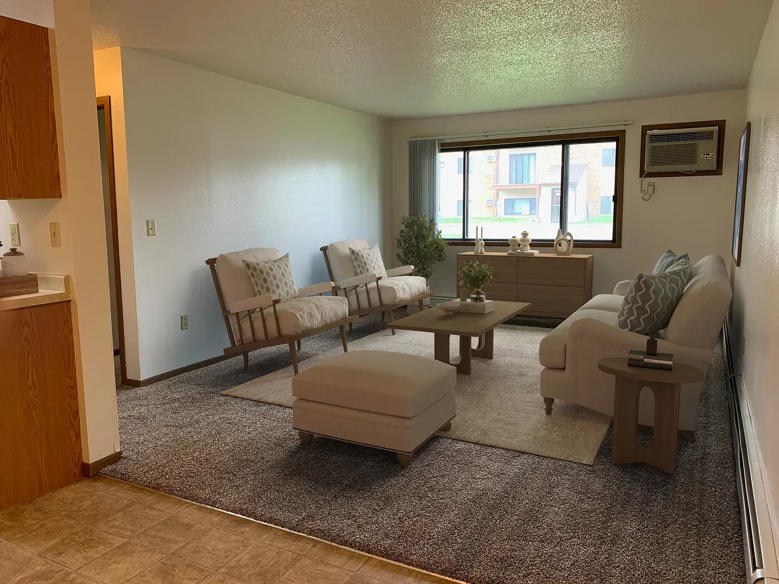 Living room with beige furniture, a rug, and a window overlooking an apartment complex.
