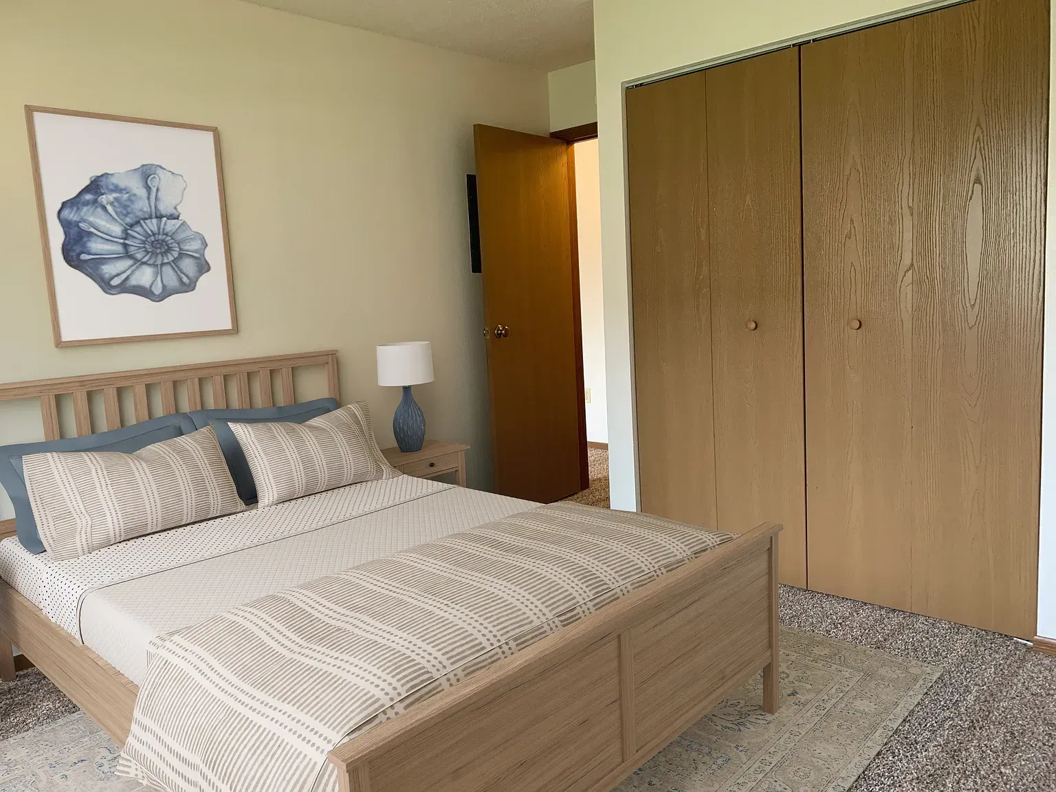 Bedroom with light wood bed, large closet, artwork, and a partly open door.