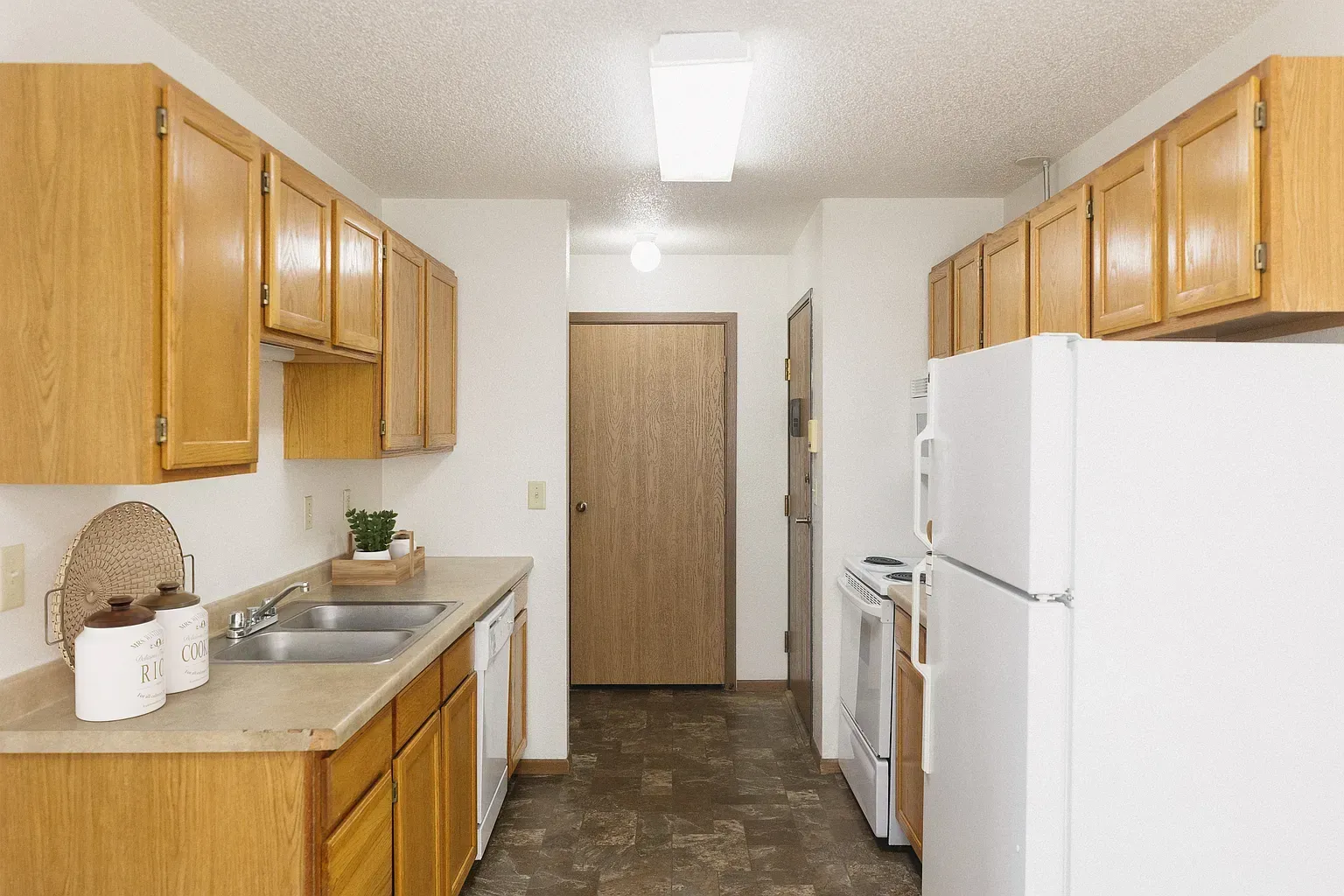Kitchen with light wood cabinets, white appliances, and a brown door.