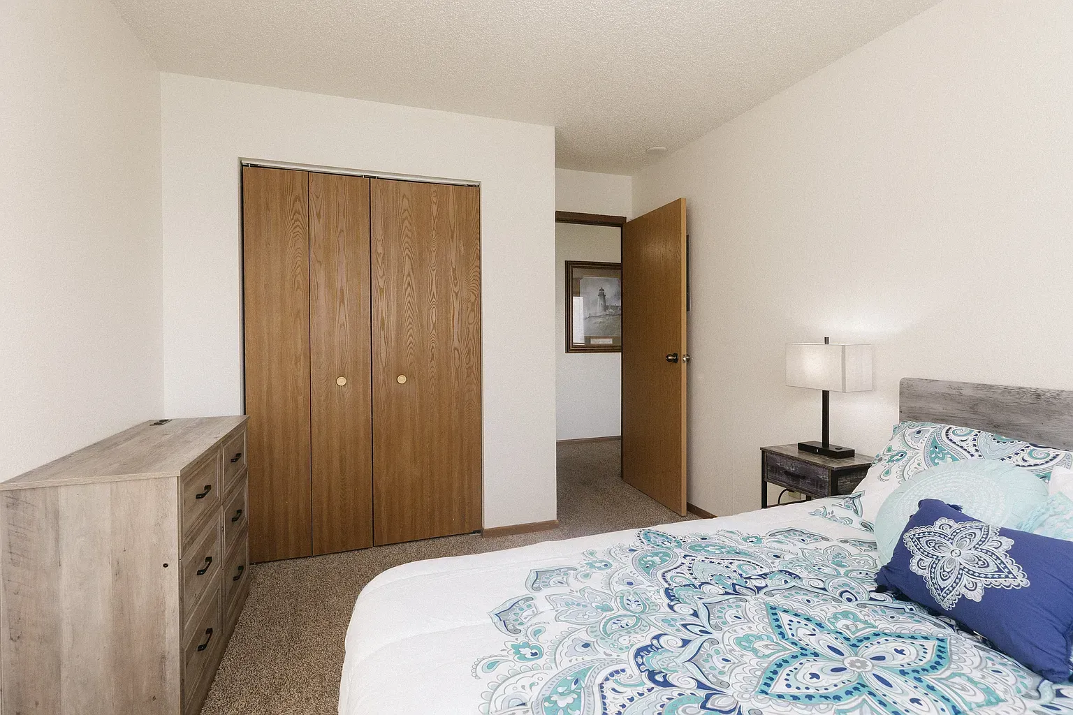 Bedroom with closet, dresser, bed with blue bedding, and a nightstand with lamp.