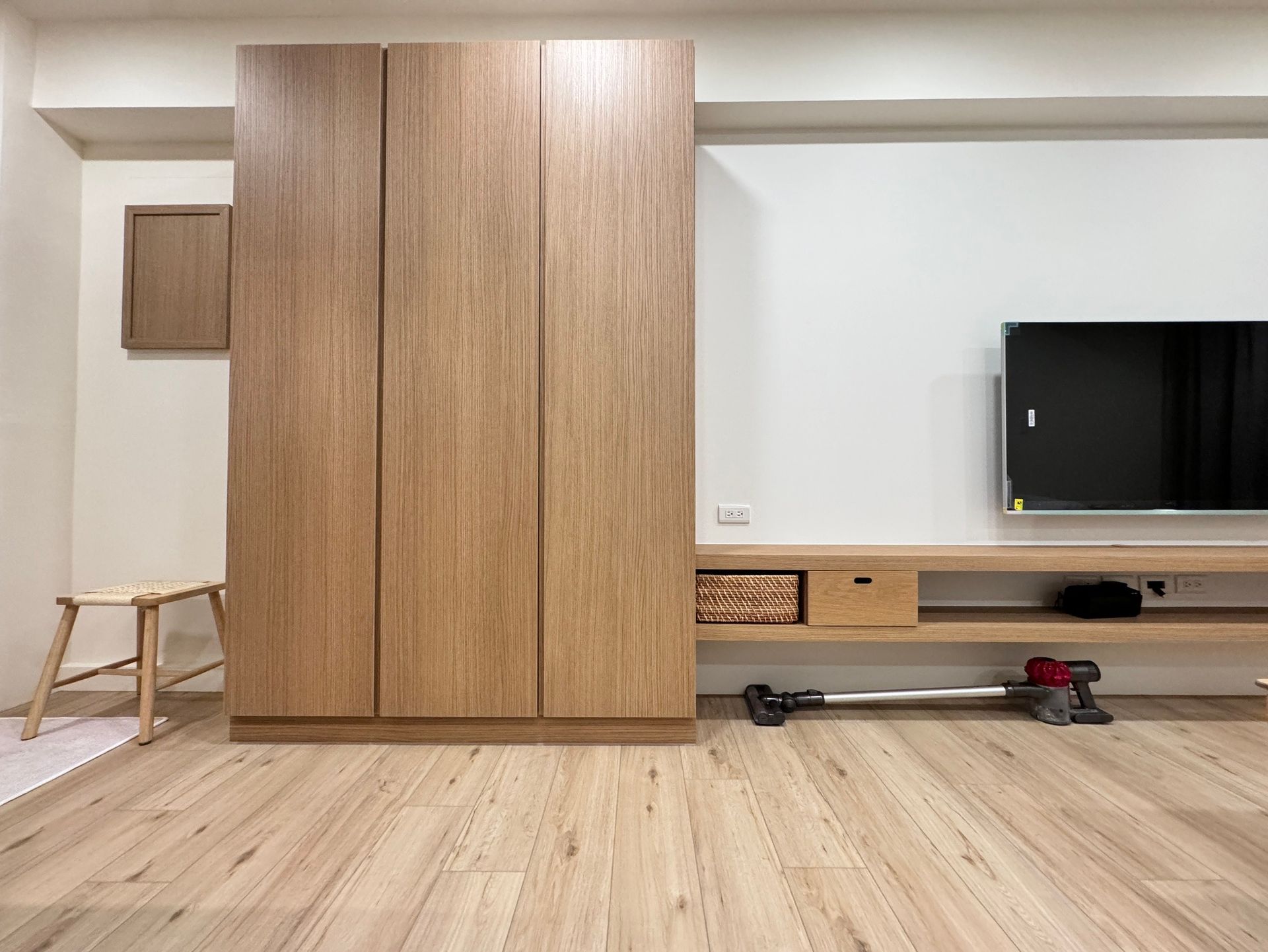 A living room with a wooden cabinet , a vacuum cleaner , and a flat screen tv.