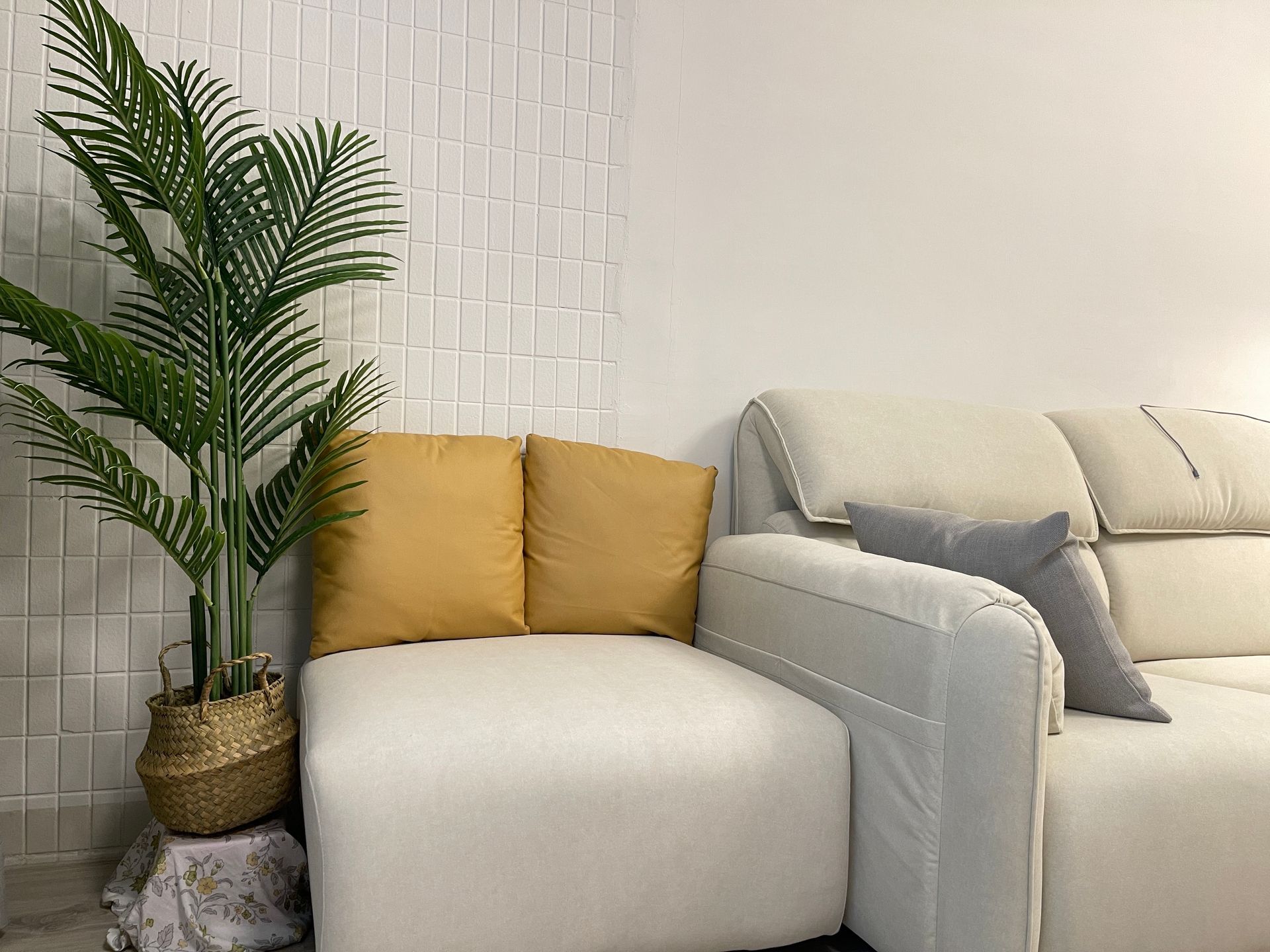 A living room with a white couch , yellow pillows , and a potted plant.