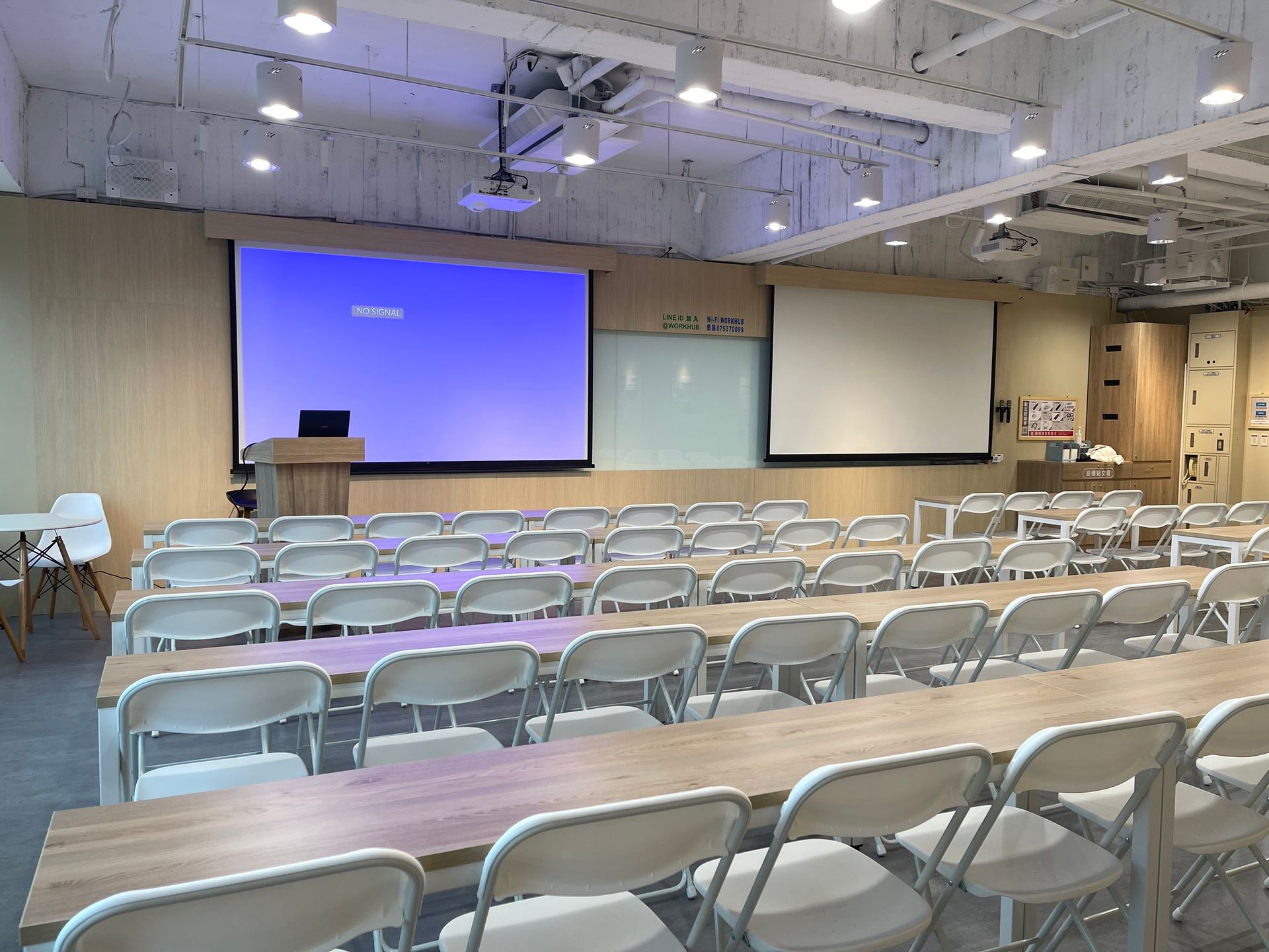 A large room with tables and chairs and a large screen.