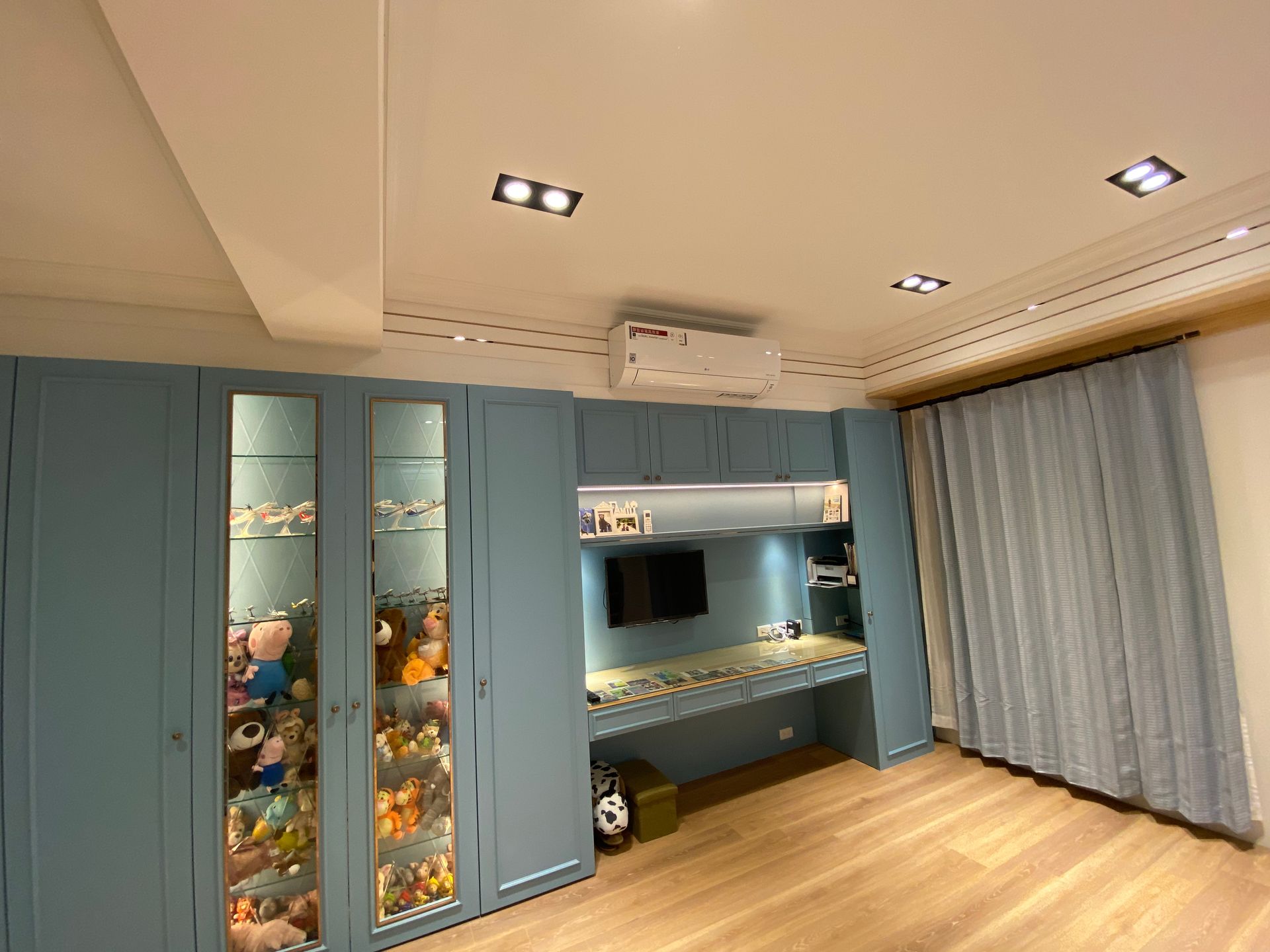 A bedroom with blue cabinets , a desk , a television and a shelf filled with stuffed animals.