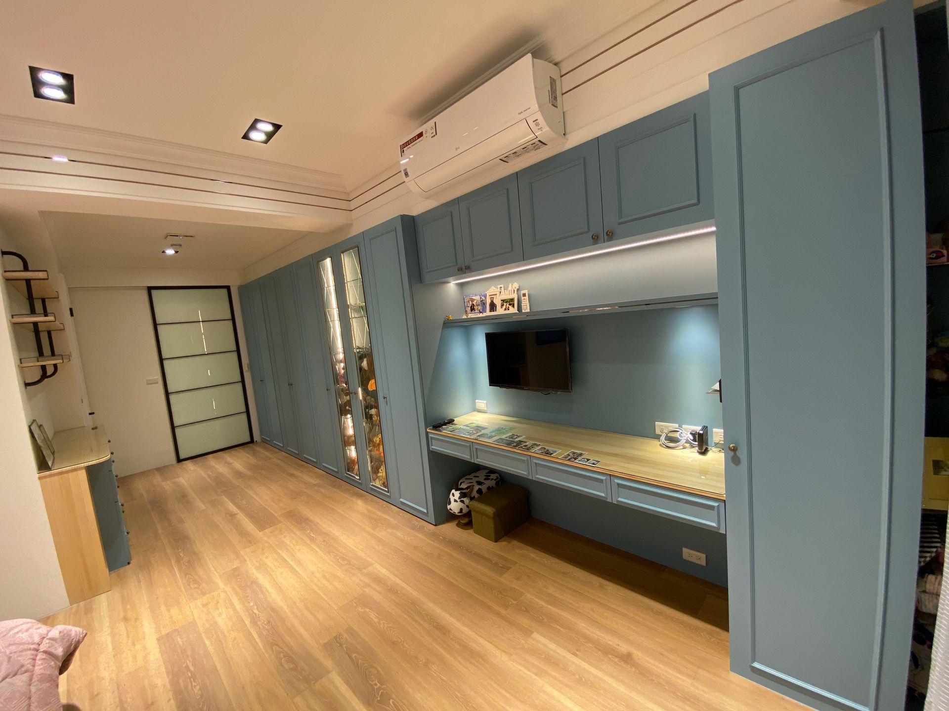 A living room with a desk and a television on the wall.