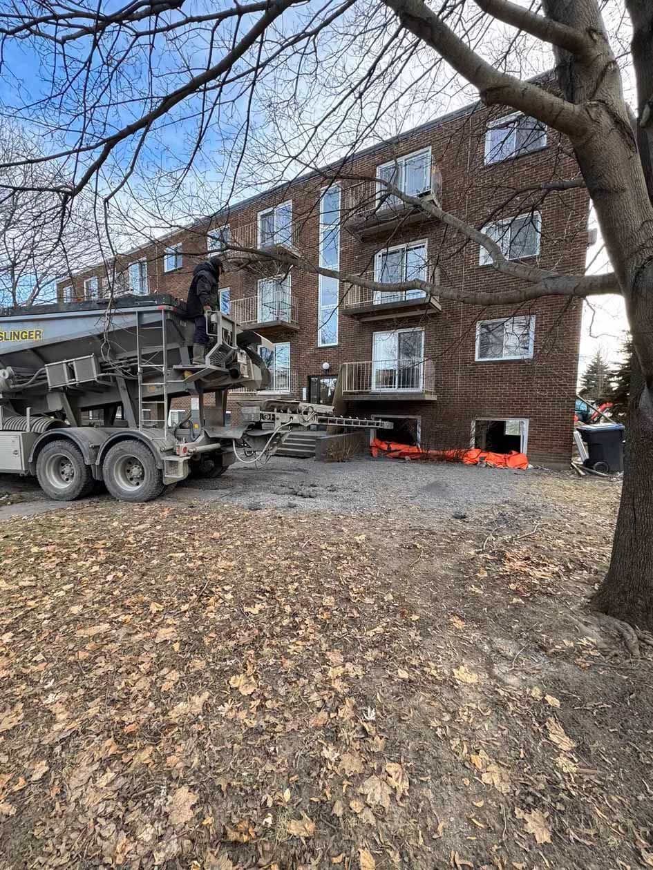 Un camion de ciment verse du béton devant un grand bâtiment en briques.