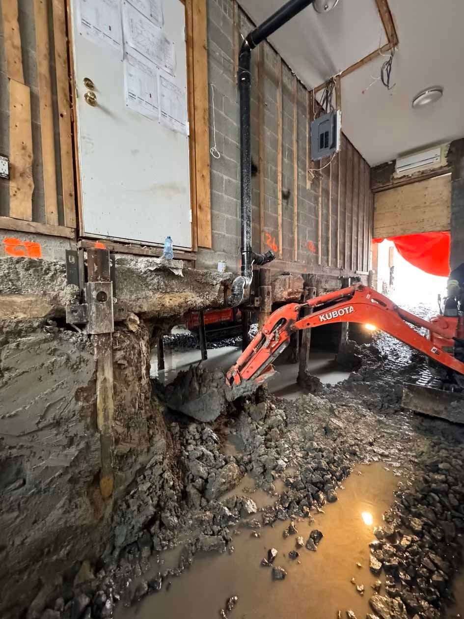 Une petite excavatrice creuse un trou dans un bâtiment.