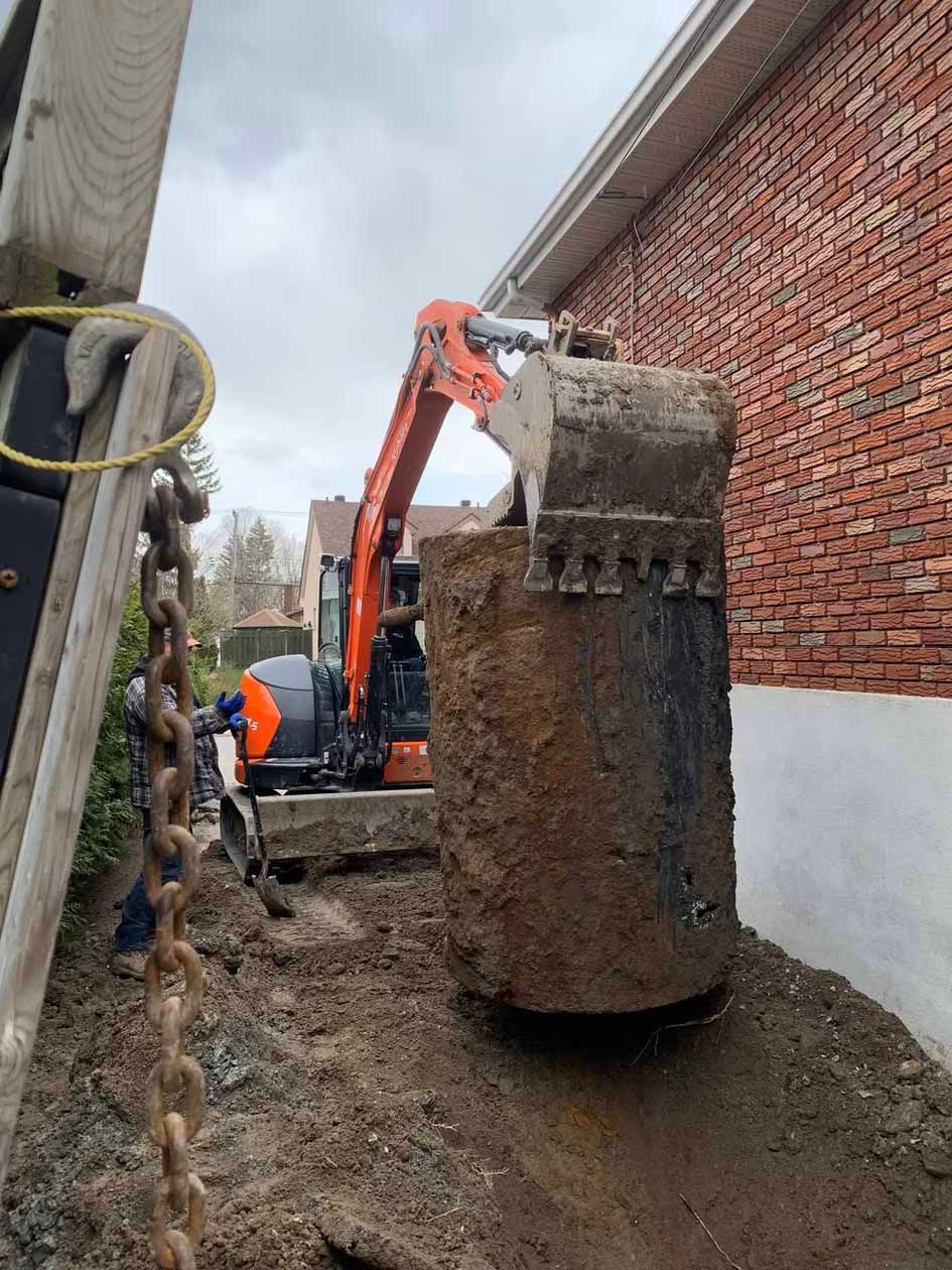 Une excavatrice creuse un trou devant un bâtiment en briques.