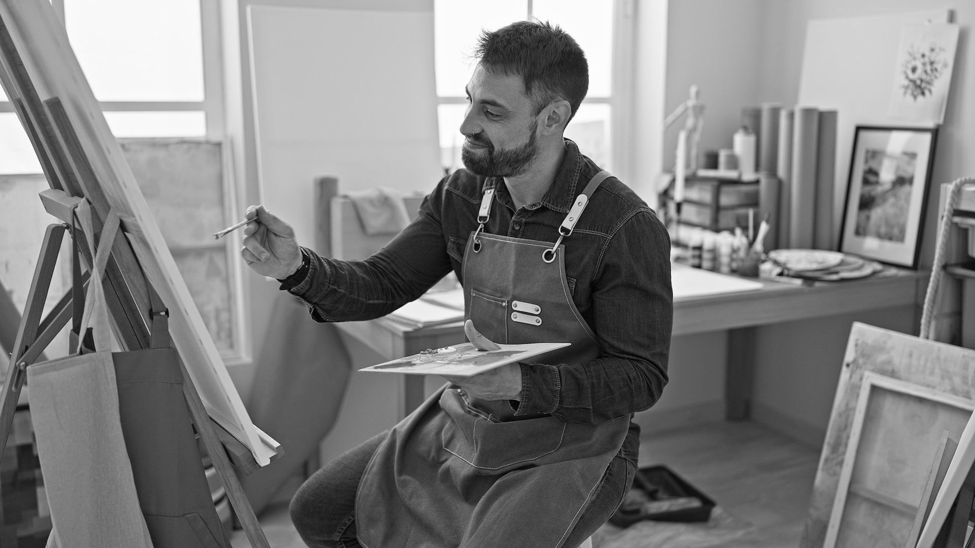 A man is sitting at an easel painting a picture.