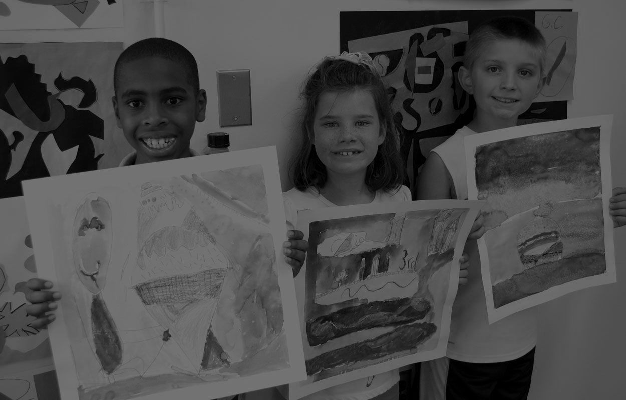 Three children are holding up their drawings in front of a wall.