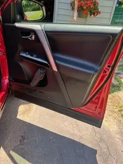 A red car with the door open is parked in a driveway.
