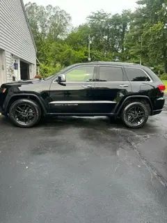 A black jeep grand cherokee is parked in a driveway in front of a house.