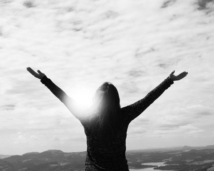 A woman is standing on top of a mountain with her arms outstretched.