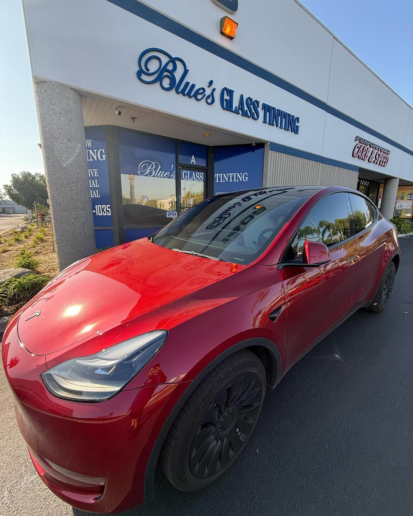 Red Tesla Y model car parked outside of Blue's Glass Tinting storefront.
