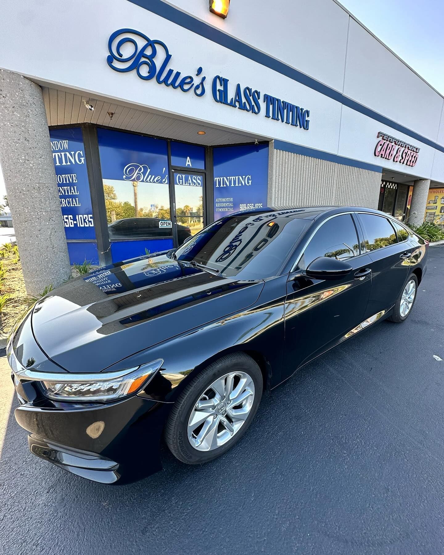 Black car with tinted windows parked in front of a Blue's Glass Tinting storefront.