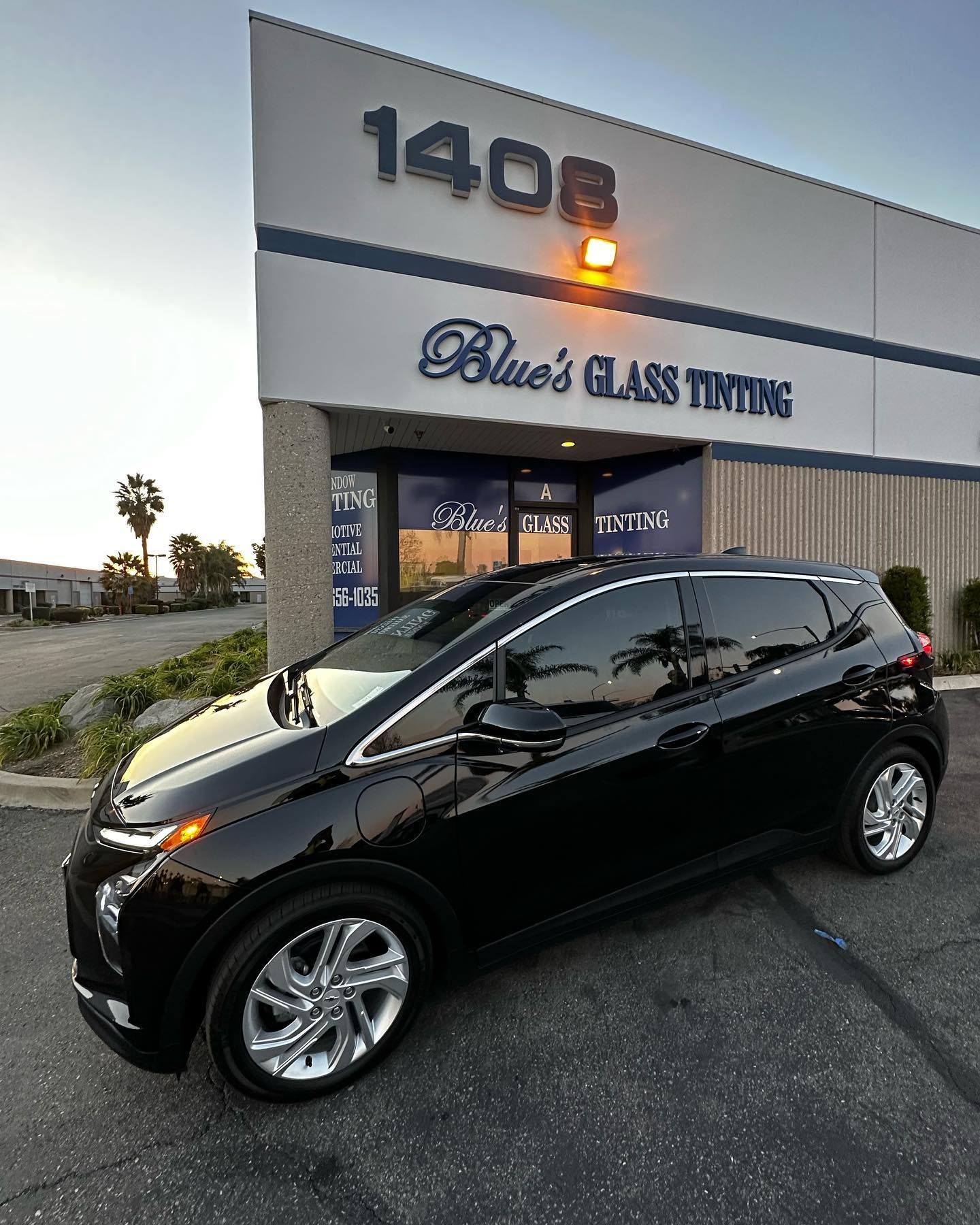 Black car with tinted windows parked in front of a building with glass tinting sign.