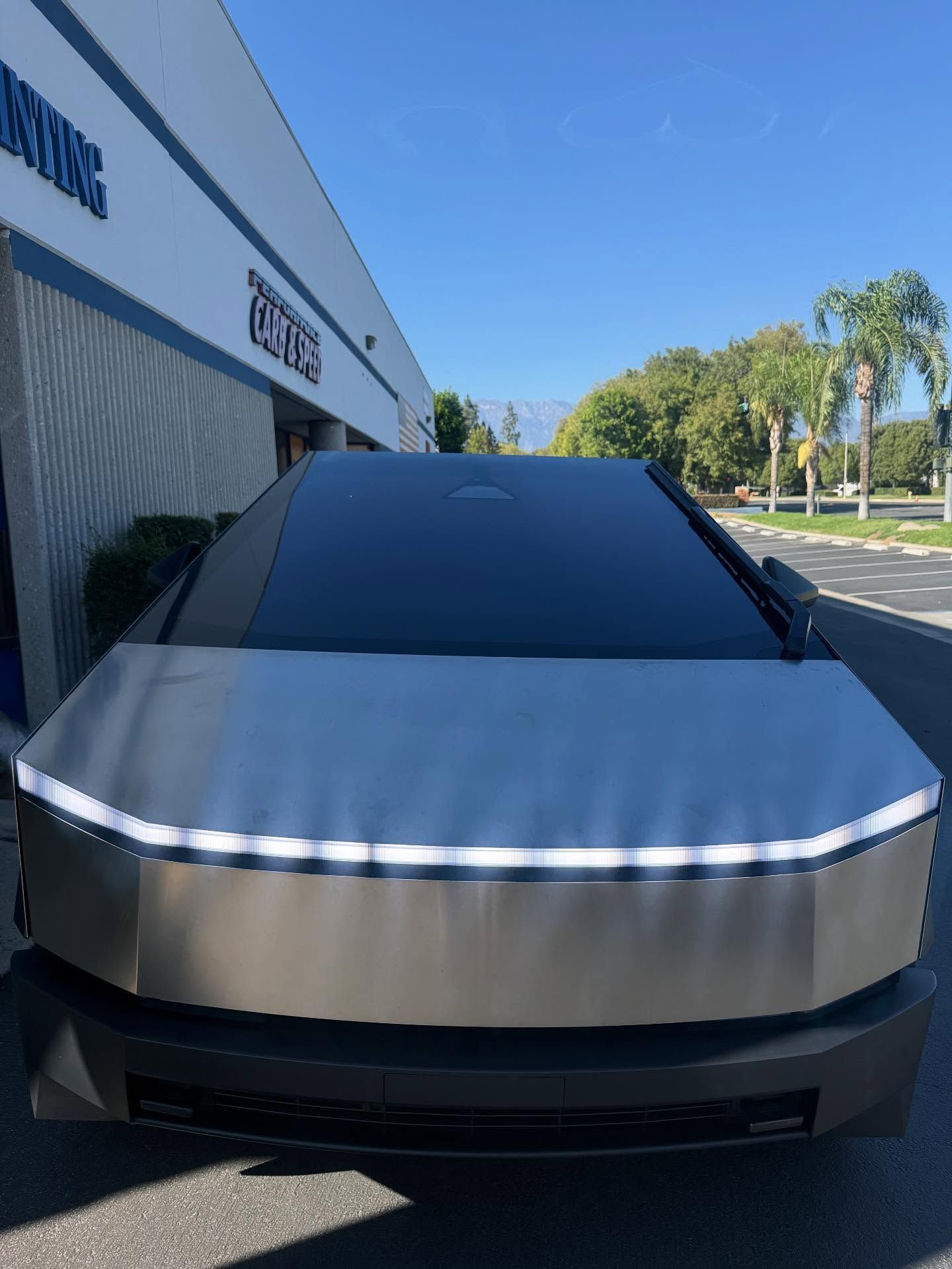 Tesla Cybertruck parked in front of a building with a blue sky and palm trees in the background.