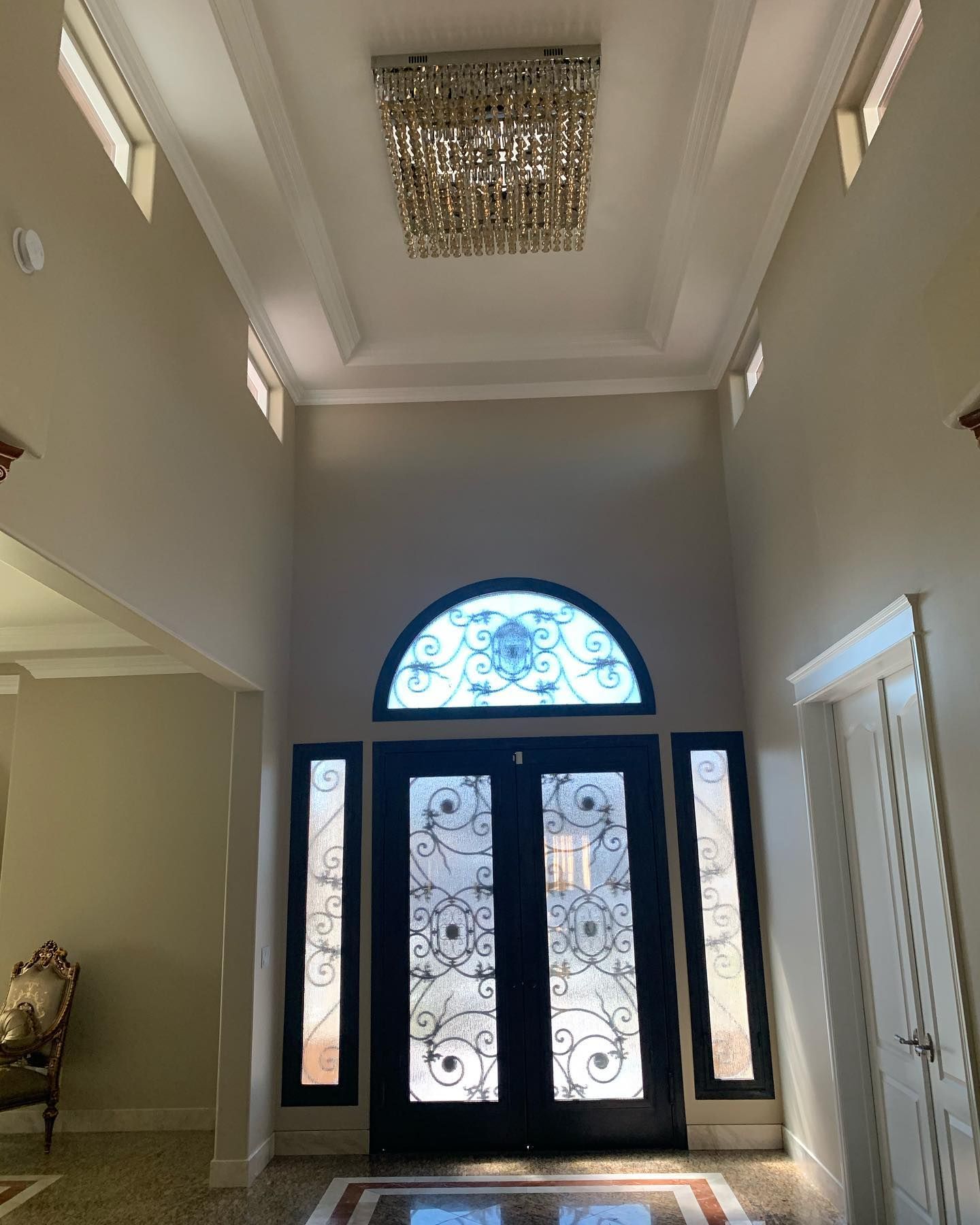 Grand entrance hall with tall ceiling, chandelier, ornate doors, and sidelights.